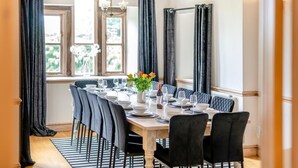 Ein Esszimmer mit einem langen Tisch, gedeckt für sechs Personen, dunklen Vorhängen und einem Fenster mit Aussicht.