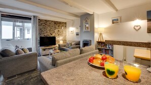 Una sala de estar con pared de piedra, un televisor de pantalla plana, chimenea y un comedor con fruta y bebidas.