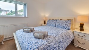 Un dormitorio con una cama grande, dos mesitas de noche, un ventanal y un radiador.