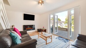 Sala de estar con chimenea, un sofá, una mesa de centro y vistas a través de grandes puertas correderas de vidrio.