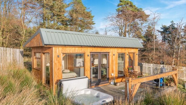 En træhytte med metal tag, en jacuzzi og en terrasse med udendørs møbler.