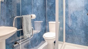 Un baño con un lavamanos blanco, un inodoro, una cabina de ducha de vidrio y una pared de mármol azul.