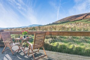 A wooden deck with two chairs and a table, overlooking a grassy field with a wooden fence and distant hills. - 1 Bed in Newton In Bowland (oc-h34064) (Newton)