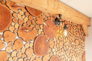 A wall of stacked logs with a wooden beam ceiling and two wall-mounted light fixtures.