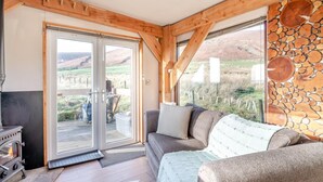 A cozy cabin interior with a fireplace, a sofa, and a large window offering a view of the outdoors. - 1 Bed in Newton In Bowland (oc-h34064) (Newton)