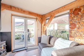 A cozy cabin interior with a fireplace, a sofa, and a large window offering a view of the outdoors. - 1 Bed in Newton In Bowland (oc-h34064) (Newton)