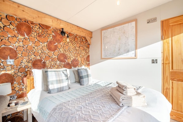 Une chambre avec un mur en pierre, un lit avec une couette, des oreillers, une table de chevet avec une lampe et une carte accrochée au mur.