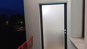 Eine moderne Tür mit einem satinierten Glasfenster, einem roten Metallgeländer und einer kleinen Ablage mit einer Leuchte.