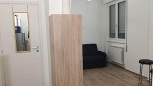 Ein Zimmer mit Holzboden, einem schwarzen Stuhl, einer Heizung und einem Fenster mit Jalousien.