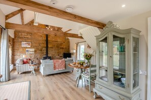 Ein gemütliches Wohnzimmer mit Steinwand, Holzbalken, Kamin, einem Esstisch mit Stühlen und einem Vintage-Schrank.