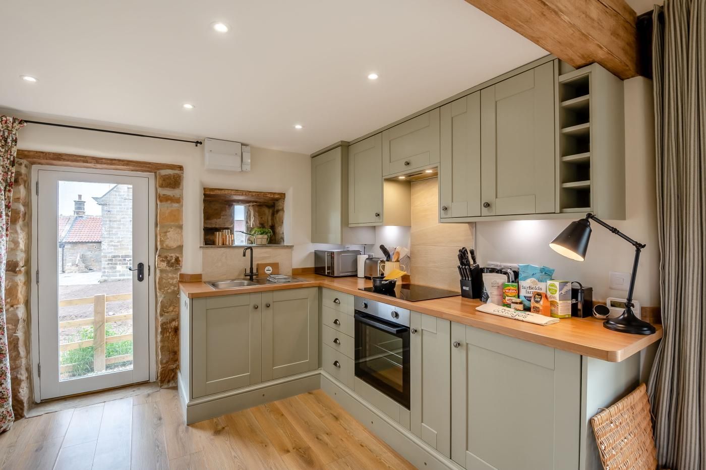 Une cuisine moderne avec des meubles gris, un plan de travail en bois et un four encastré.
