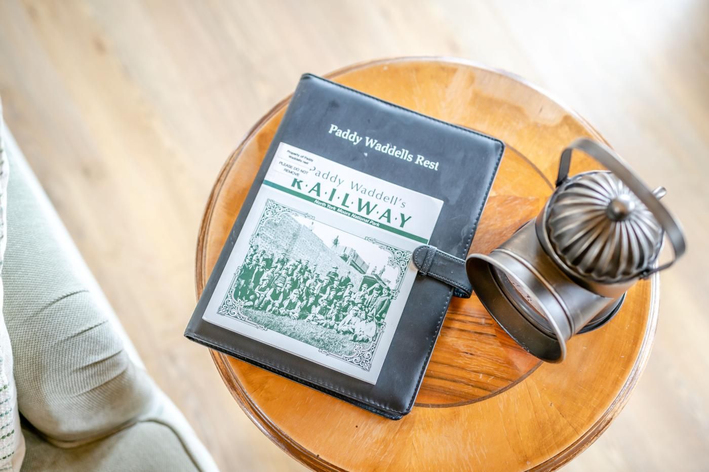 Um livro intitulado 'Paddy Waddell's Railway' sobre uma mesa de madeira redonda com um objeto de metal ao lado.
