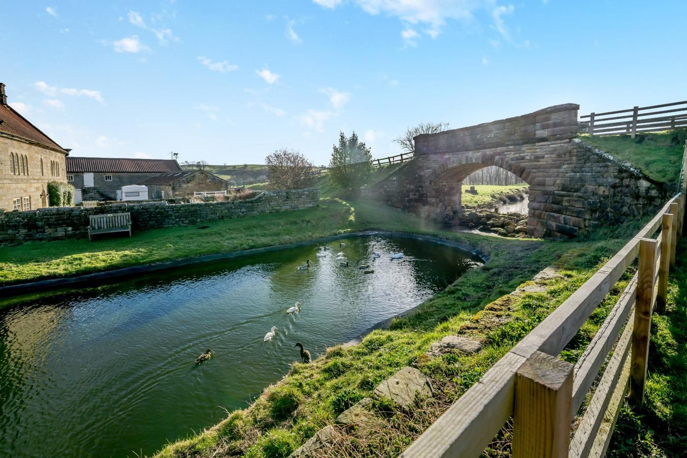 A canal with ducks, a stone bridge, and a wooden fence.