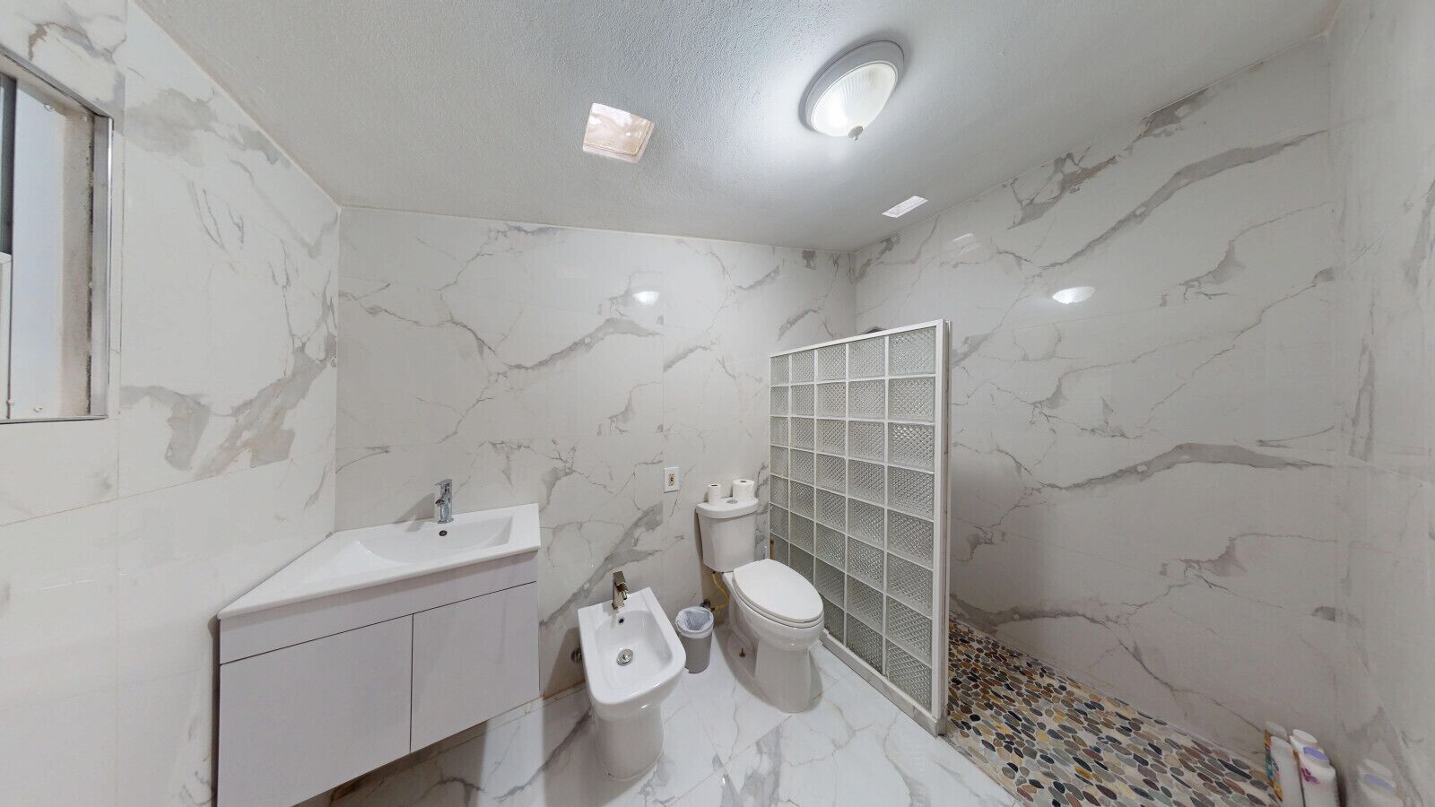 A bathroom with a marble sink, toilet, bidet, and a shower with a glass door.