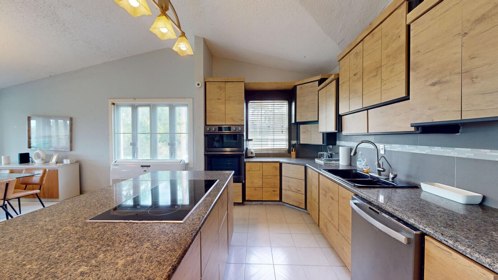 A modern kitchen with granite countertops, wooden cabinets, a built-in oven, and a large island with a stovetop.