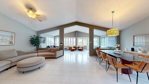 Amplia sala de estar con un sofá grande, una mesa de comedor con sillas y una cocina visible a través de un arco abierto.