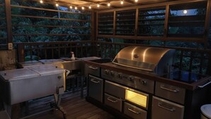 Una cocina exterior con una parrilla de acero inoxidable, horno empotrado y pileta.