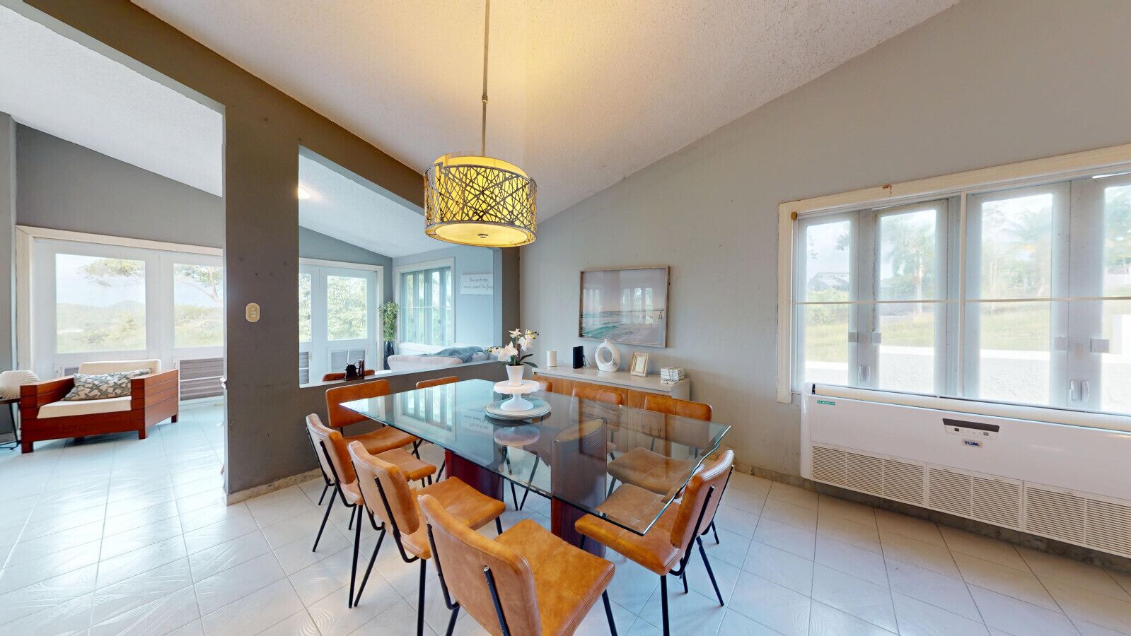 A modern dining area with a glass table, leather chairs, and a hanging light fixture.