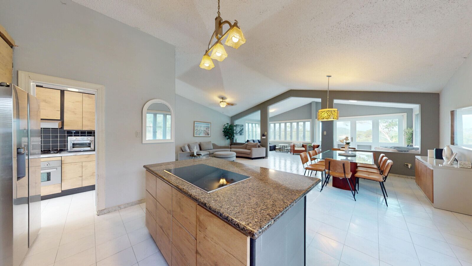 A spacious kitchen with a central island, a dining area with chairs, and a large window providing natural light.