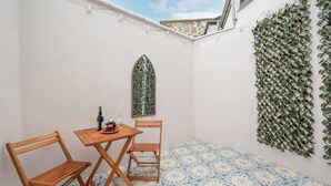 Pieni patio, jossa on pöytä ja kaksi tuolia, koristeellinen seinä, jossa on viherkasveja, ja kuvioitu lattia.