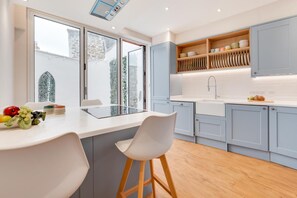 Een moderne keuken met een centraal eiland, witte barkrukken en een ingebouwde oven.