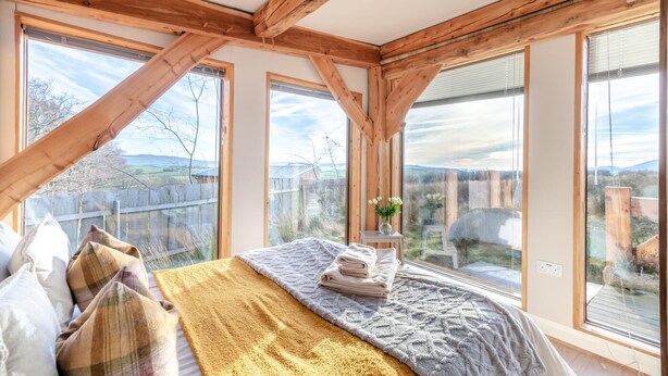 Quarto com uma cama grande, vigas de madeira e várias janelas com vista para o exterior.