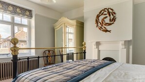 Een slaapkamer met een bed, een radiator, een raam met uitzicht, een spiegel en een decoratie aan de muur.