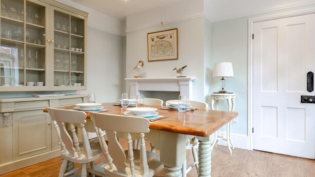 Een eethoek met een houten tafel, witte stoelen en een kast met glazen deuren.