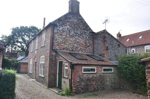 A stone house with a sloped roof, a chimney, and a small attached structure with windows. - 2 Bed in Holt (oc-1863) (Holt)