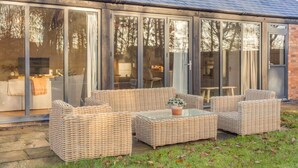 Een overdekt terras met rieten meubels en een glazen tafel.