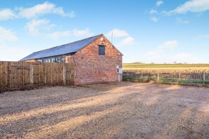 Une grange en briques surmontée d’un toit en métal, avec une clôture en bois et une allée gravillonnée.
