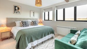 Een slaapkamer met een bed, nachtkastjes, een groene bank, een hanglamp en een uitzicht door grote ramen.
