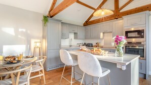 Een moderne keuken met grijze kastjes, een centraal eiland met barstoelen, een eethoek met een ronde tafel en stoelen, en een hangende plant.