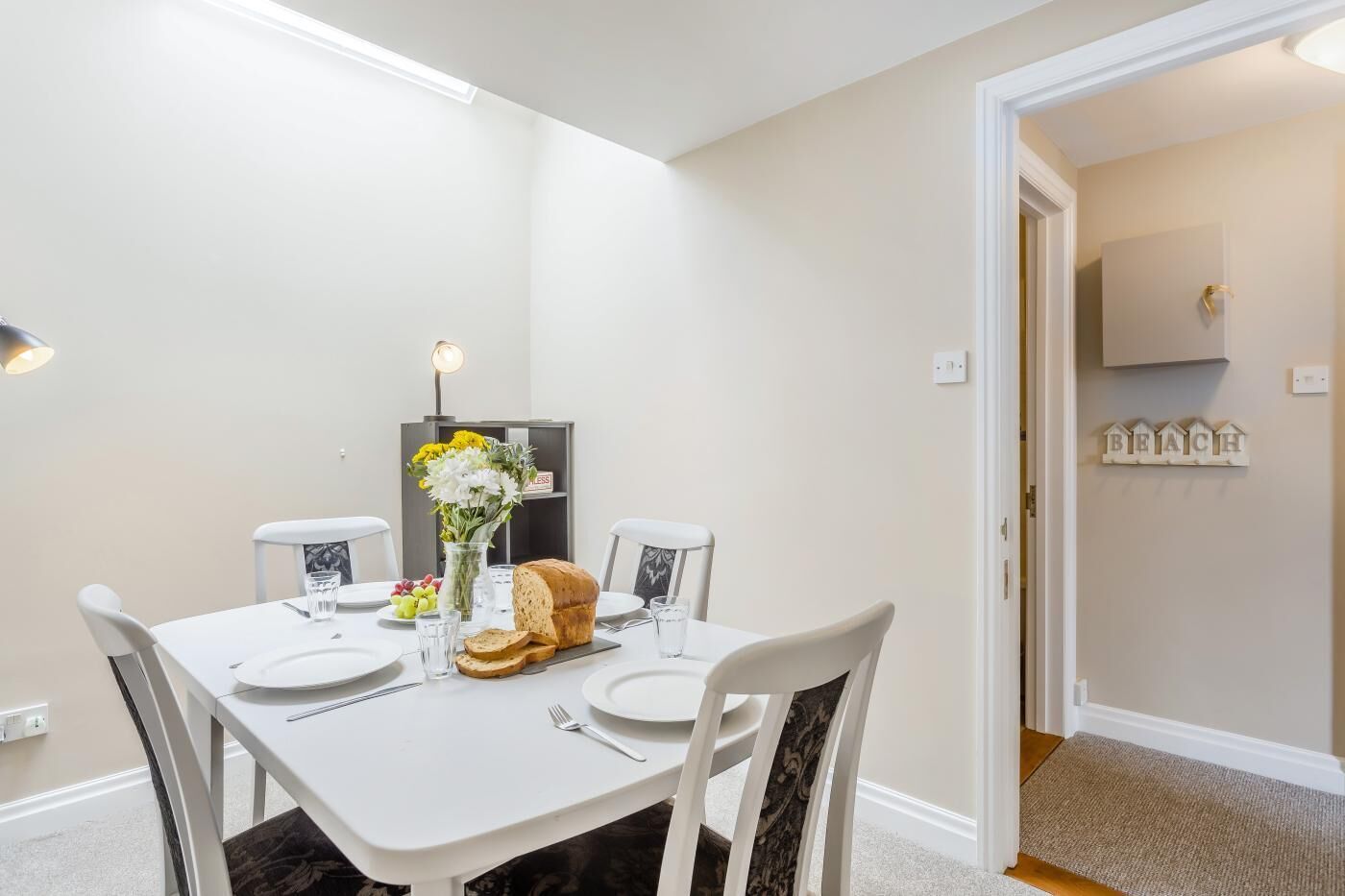 Een eethoek met een witte tafel, stoelen, een bloevas en een brood.