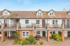 A two-story residential building with a balcony, a small garden, and a door with a number. - 2 Bed in Aldeburgh (oc-mst) (Aldeburgh)