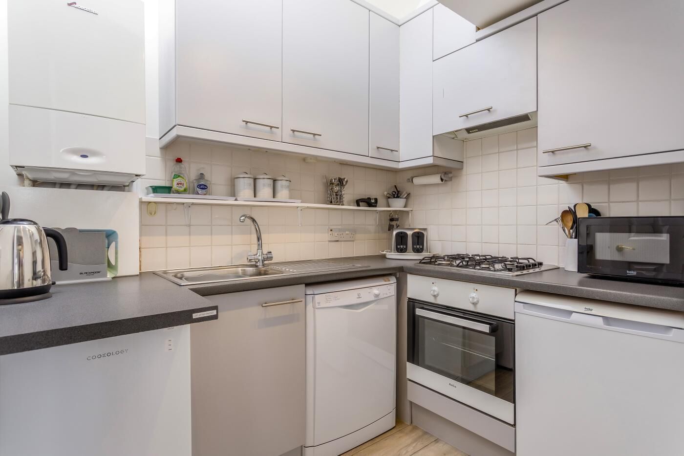 Cocina compacta con armarios blancos, lavavajillas integrado, estufa y microondas.