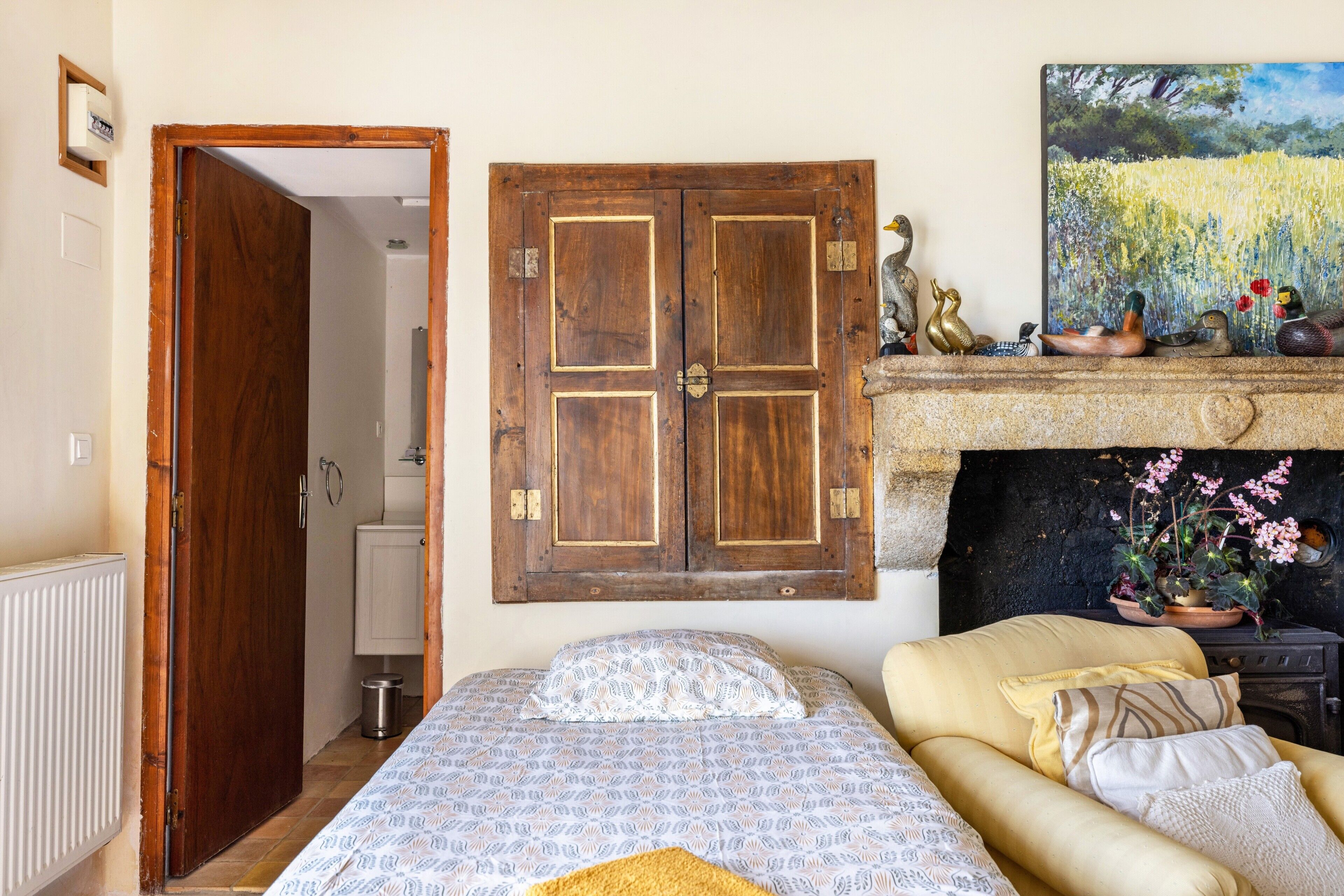 Een slaapkamer met een bed, een bank, een houten kledingkast, een schilderij en een open haard.