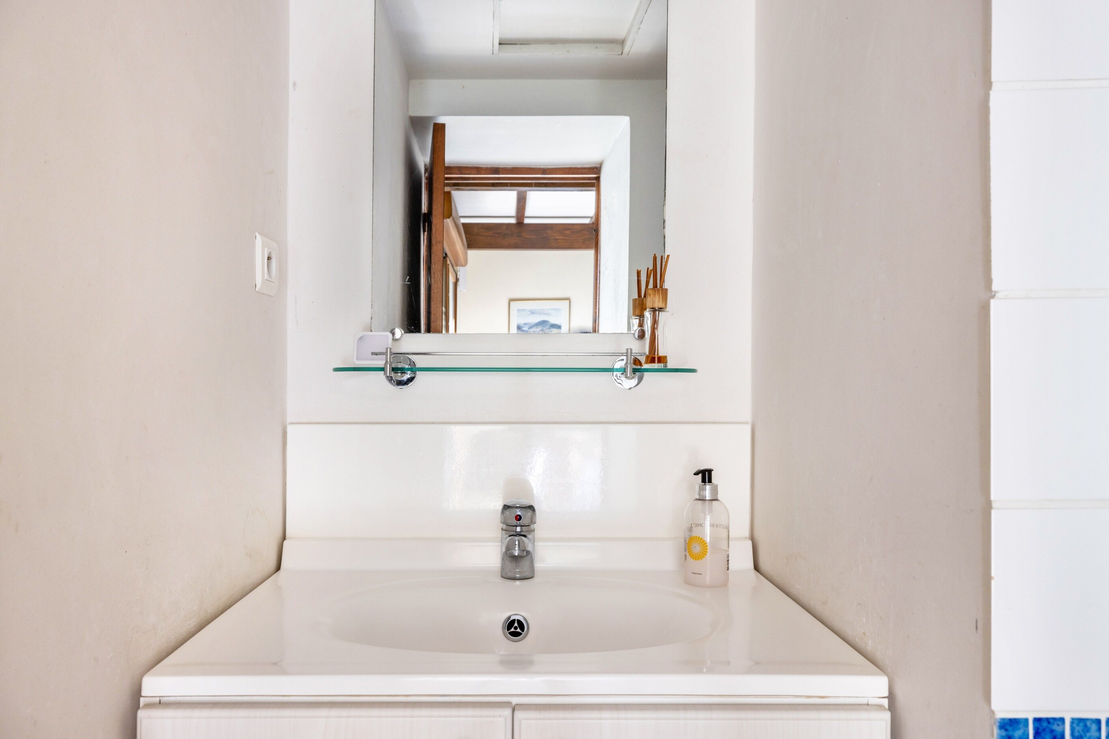 Un baño con un lavamanos blanco, un espejo encima y una puerta de madera al fondo.