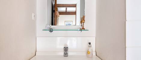 Un baño con un lavamanos blanco, un espejo encima y una puerta de madera al fondo.