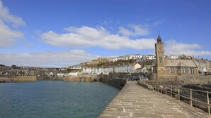 A coastal town with a prominent clock tower, stone buildings, and a stone quay extending into the water.