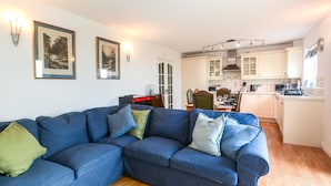 A living room with a blue sofa, a dining area with a table and chairs, and a kitchen with white cabinets.