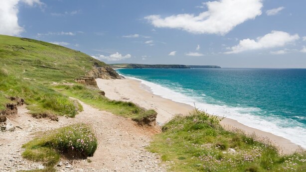 A coastal path leading to a beach with a clear view of the ocean and distant cliffs.