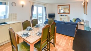 A dining area with a wooden table set for four, a blue sofa, and a television in the background.
