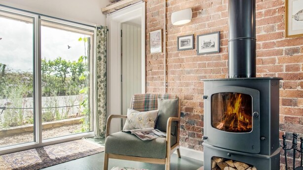 Un cuarto acogedor con chimenea, un sillón cómodo, vistas a través de un ventanal y una pared de ladrillo.