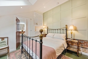 A bedroom with a bed, a nightstand, a lamp, a chair, and a door.