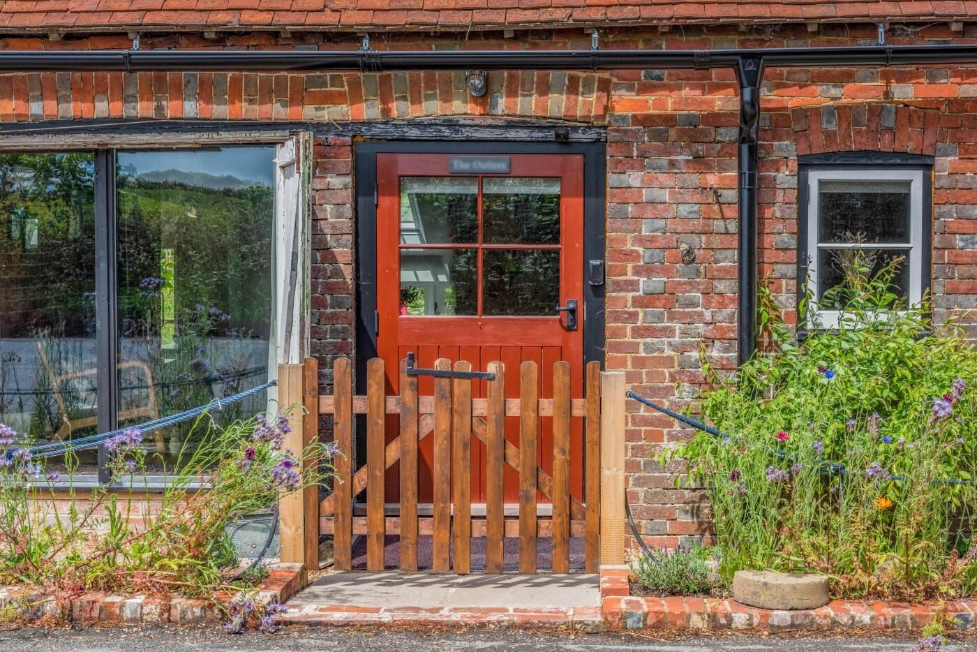 A brick building with a red door, a wooden gate, and a window.