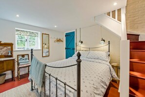 A bedroom with a bed, a chair, a dresser, a window, a mirror, and a staircase.