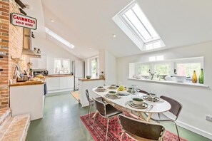 Une cuisine moderne avec un mur en briques, un coin repas avec une table dressée pour quatre personnes, et une lucarne au-dessus.