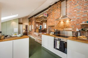 A modern kitchen with exposed brick walls, a stainless steel range hood, and a built-in oven.