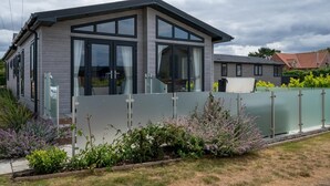 Ein modernes Haus mit großen Fenstern, einer überdachten Veranda und einem eingezäunten Garten.